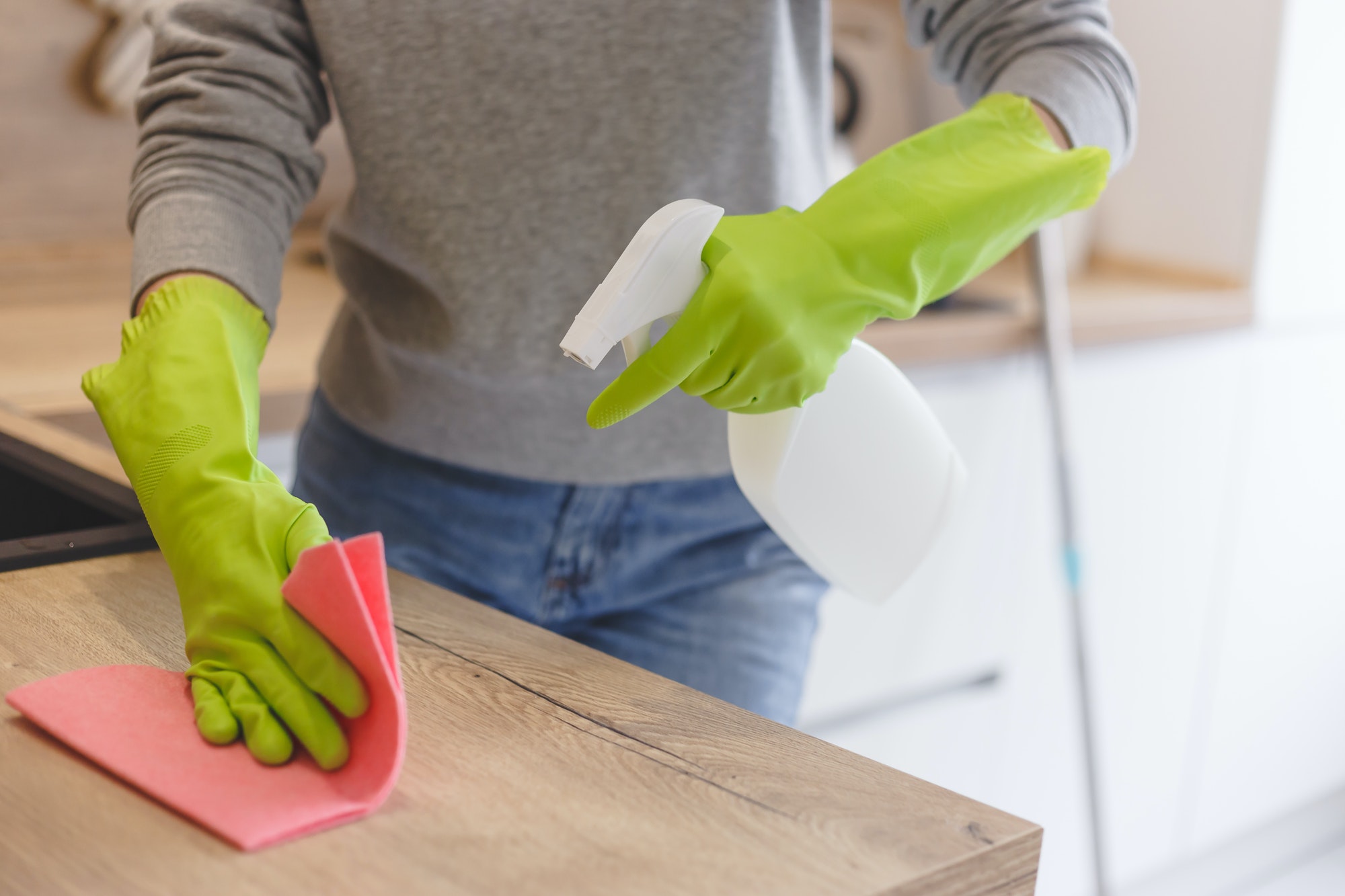 Close up woman cleaning kitchen using cleanser spray and cloth.