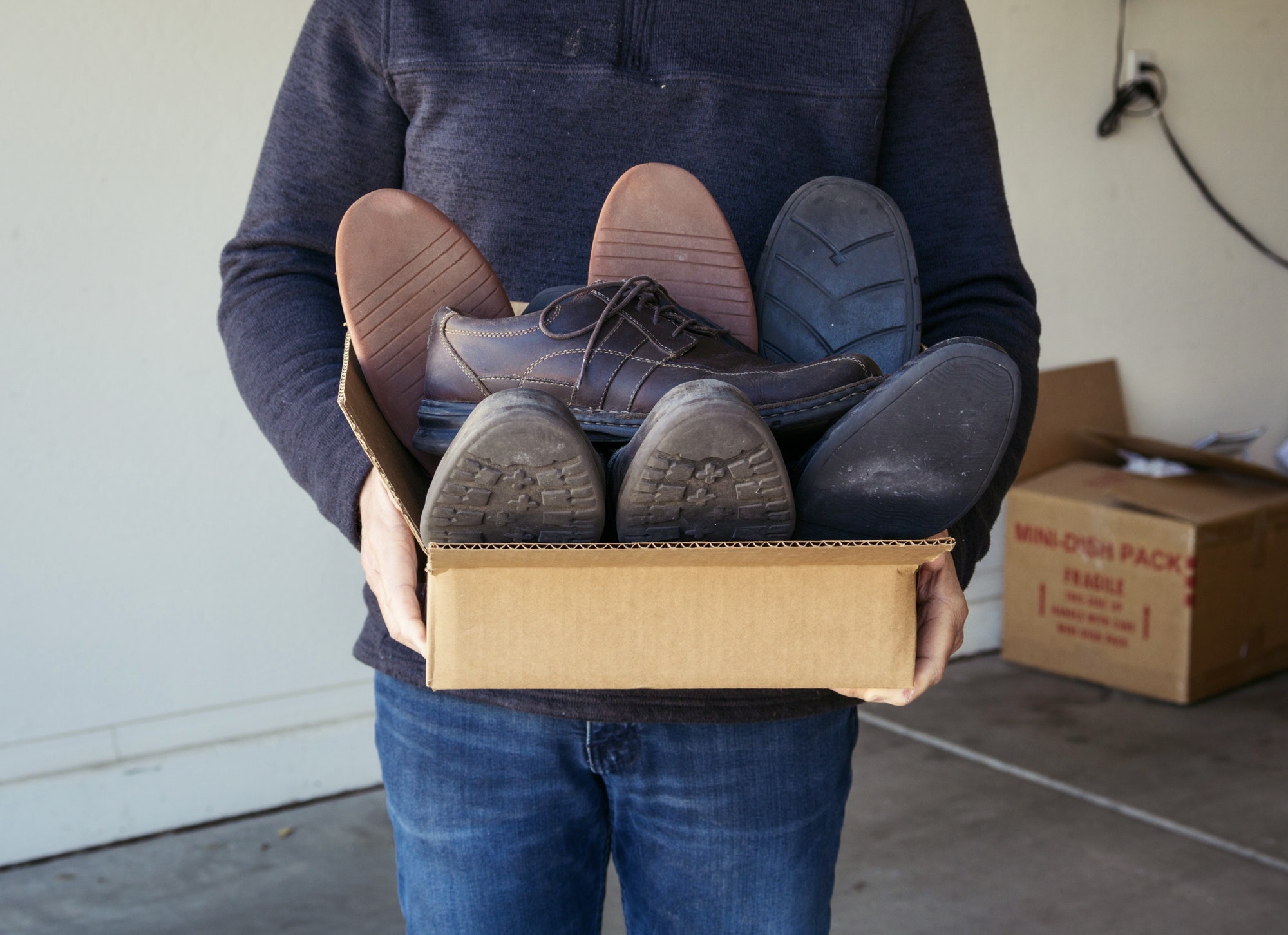 Adult male carrying a box of gently used shoes being donated to a charity organization for resale